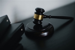 [ai] A close-up of a wooden gavel with a gold band placed on a dark surface, next to black binder files.